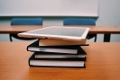 Foto von einem Bücherstapel, ganz oben liegt ein iPad auf dem Stapel und im Hintergrund leere Stühle